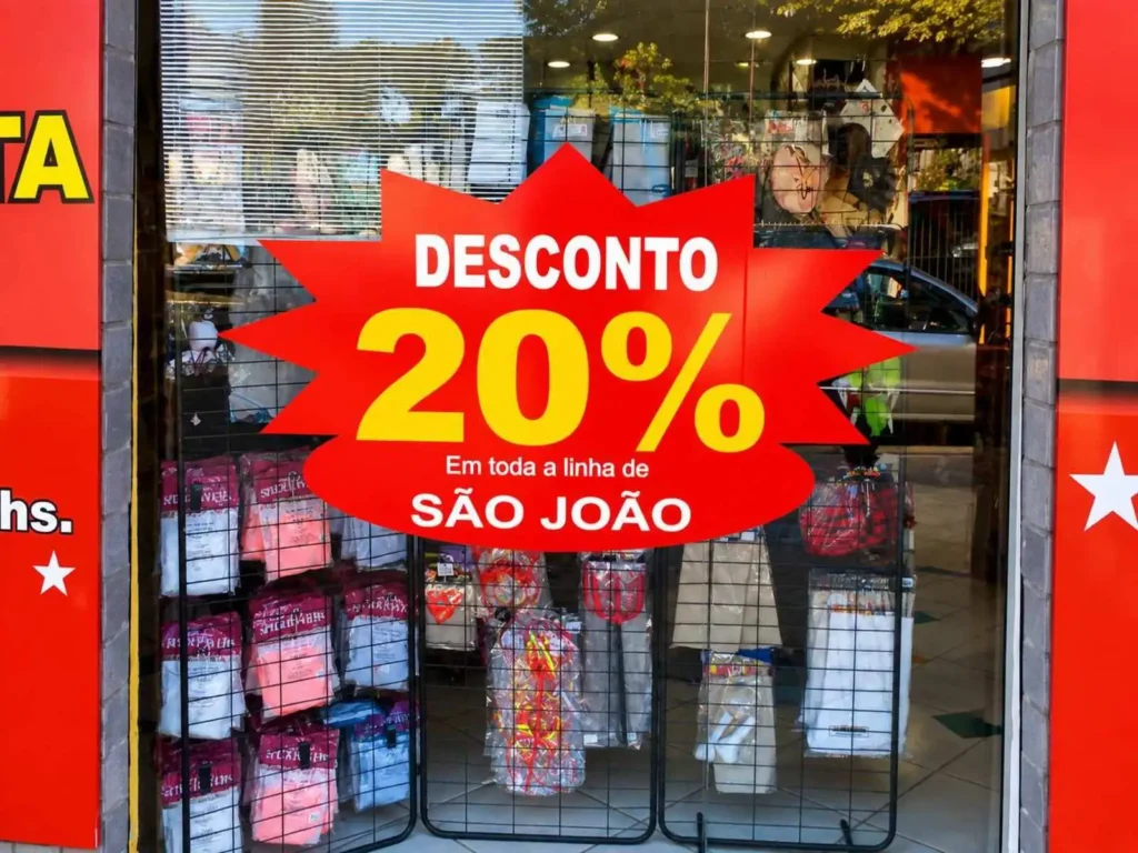 Vitrine de loja com adesivo promocional de desconto de 20 por cento na linha de São João, produzido pela Centeno Comunicação Visual.